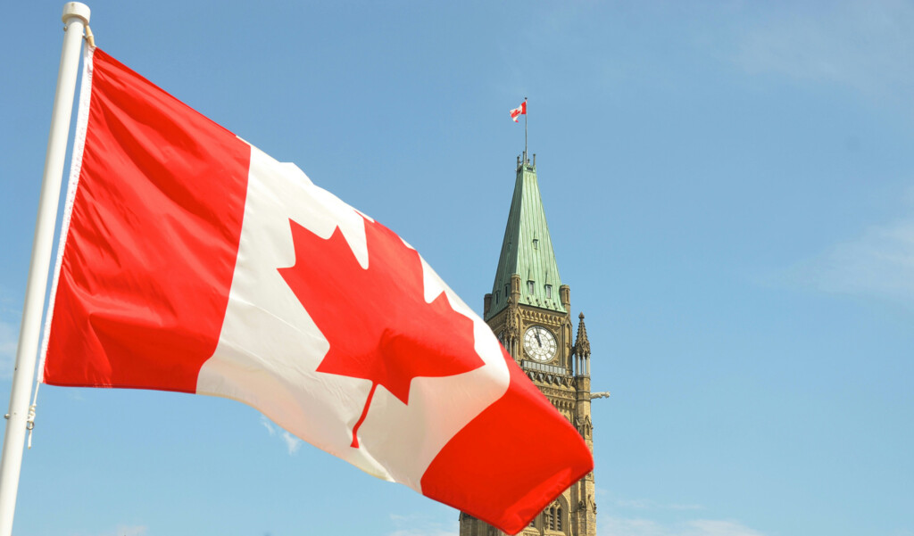 Flag of Canada waving with the Canadian Parliament Building in the background.