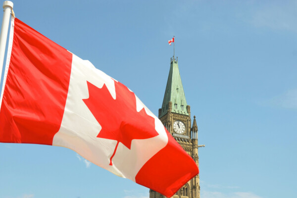 Flag of Canada waving with the Canadian Parliament Building in the background.