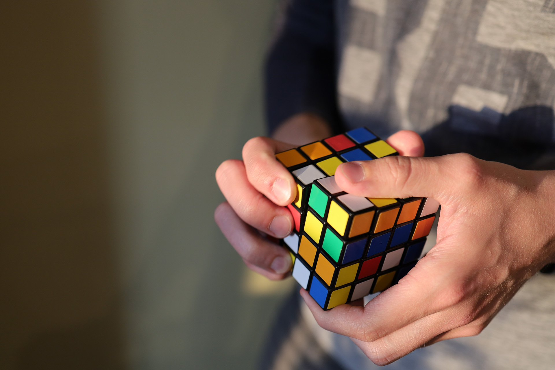 A close up of a person's hands while trying to solve a Rubik's cube puzzle.