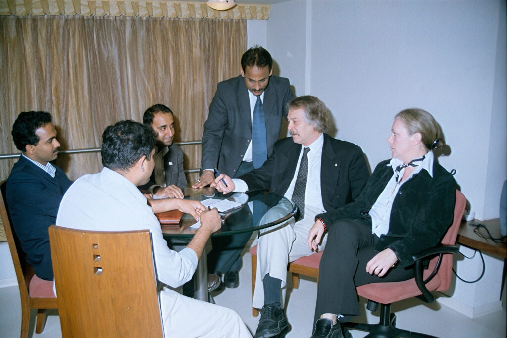 Nicolas sits with his wife, Irinela, as they meet with faculty at the Kohinoor Business School in Mumbai. There are three men sitting at the table with them, and one man standing next to Nicolas. 