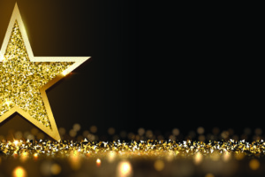 A golden star against a black background, standing on gold glitter.