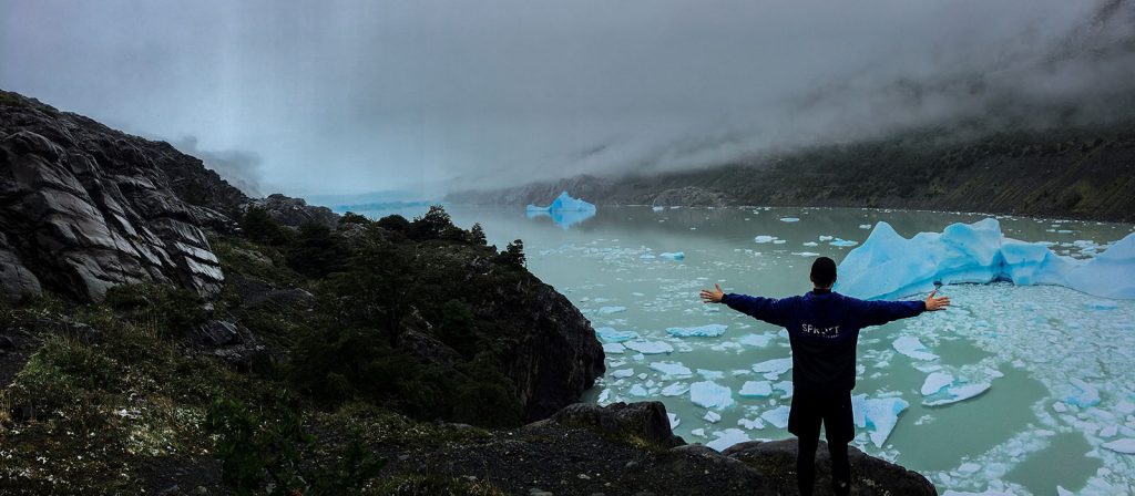 BIB student wearing a Sprott windbreaker jacket with arms spread out looking out at ice bergs in Patagonia, Chile.