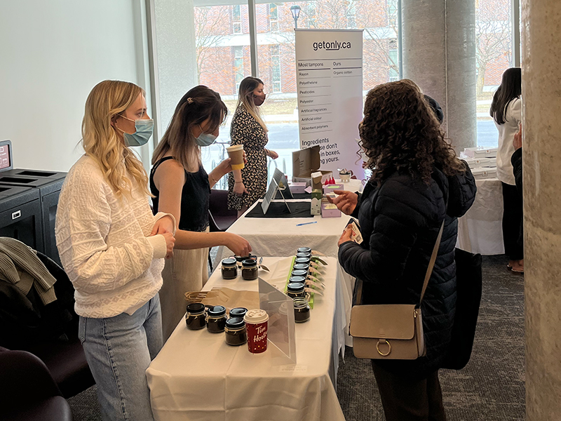 Two women standing behind a table and presenting their product to potential customers.