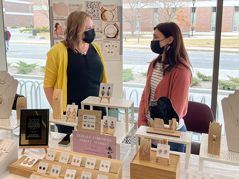 Two women in conversation behind a stand showcasing jewellery they have created.