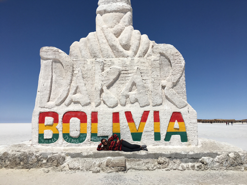 Alexandra lying down in front of a giant sign for Dakar, Bolivia.