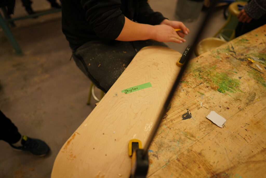 A person working on making a skateboard deck.