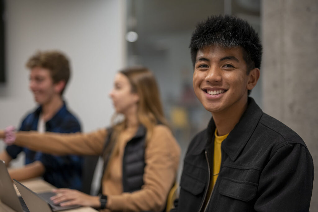 Bachelor of Commerce male student of Asian descent looking at camera while a male and female student work in the background in Carleton's Innovation Hub.