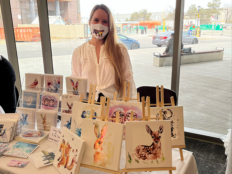 A woman standing behind a table displaying her artwork.