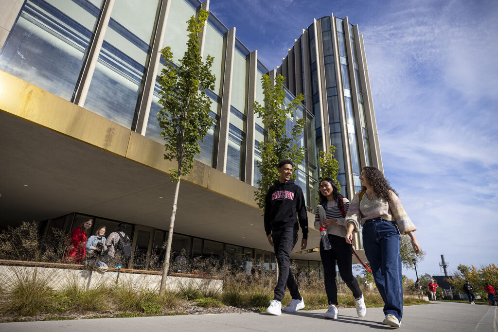 Three students smiling and conversing while walking in front of the Nicol Building, home of Carleton University's Sprott School of Business in Ottawa, Ontario, Canada.