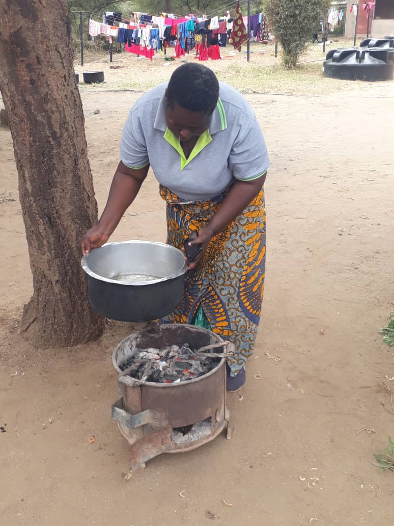 A woman holding a pot over an appliance on the ground which is emitting heat.