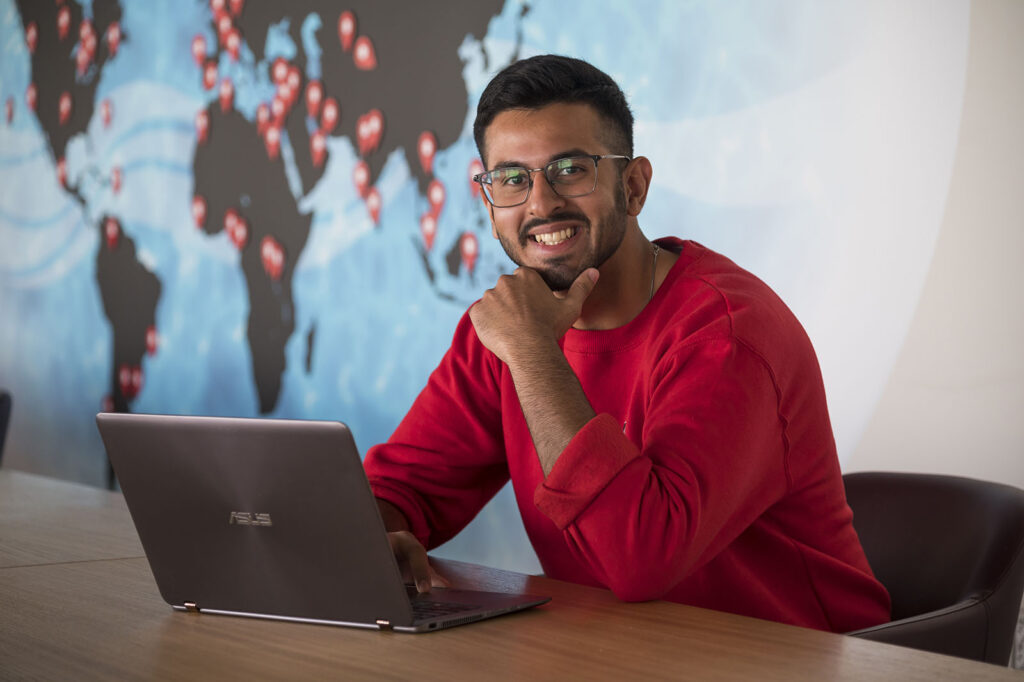Male Sprott School of Business student working on a laptop and smiling in the Undergraduate Resource Room in the Nicol Building, Carleton University in Ottawa, Ontario, Canada.