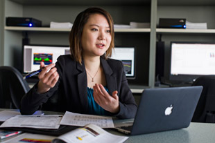 Sprott student Mimi Lam sitting at a desk with papers and a laptop on it, gesticulating with her hands