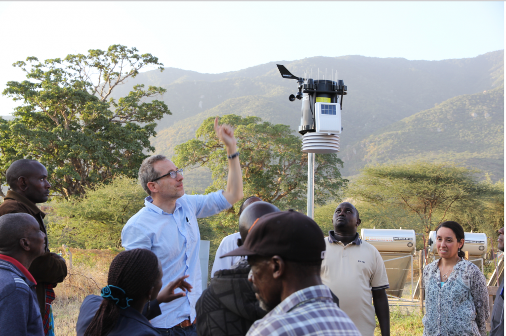 Troy Anderson with a group of people in Tanzania. He is pointing upwards at a machine as the others listen.