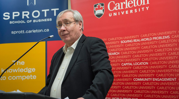 Pictured is Tony Bailetti standing in front of two banners speaking into a microphone