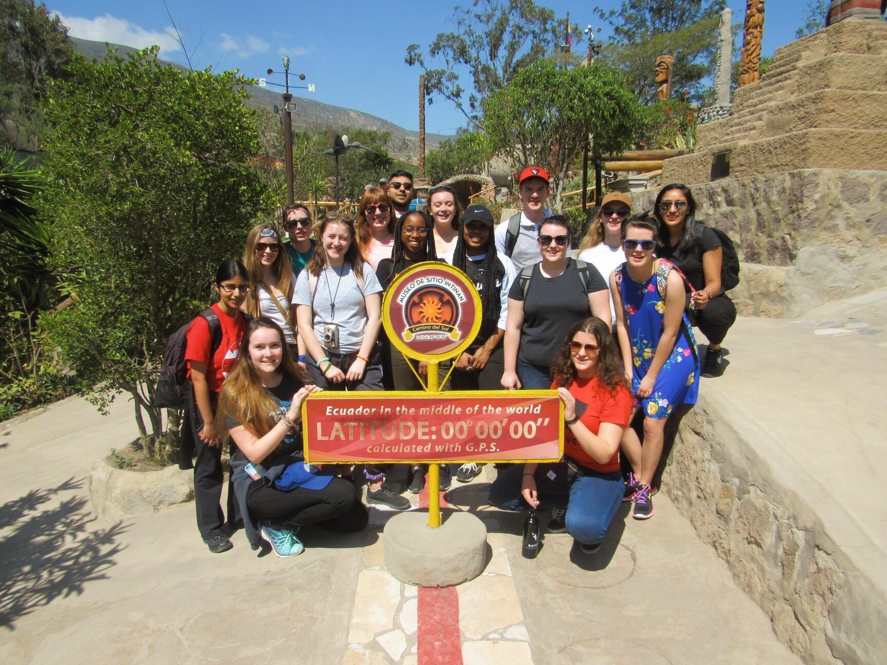 Kiana and her group members gathered around a sign that reads "Ecuador in the middle of the world".