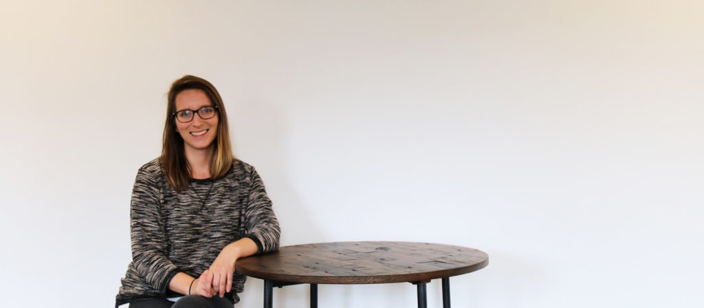 Stephanie sitting on a stool, leaning on a wood table