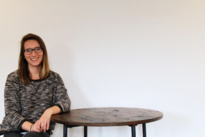 Stephanie sitting on a stool, leaning on a wood table