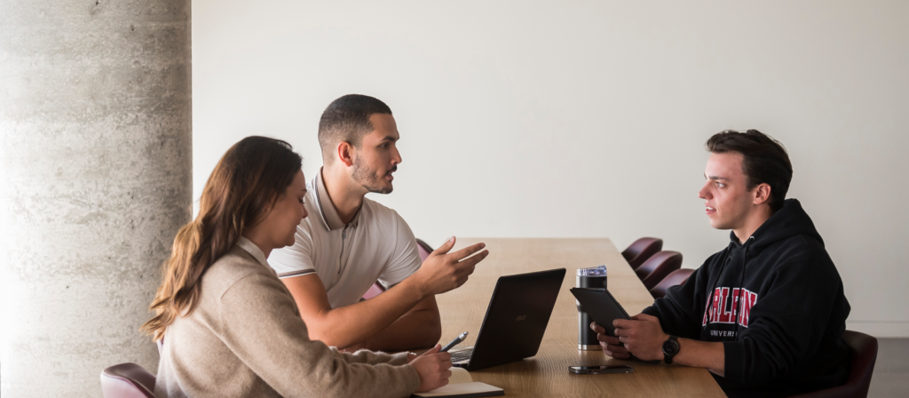 a female student and 2 male students discuss a project at a table