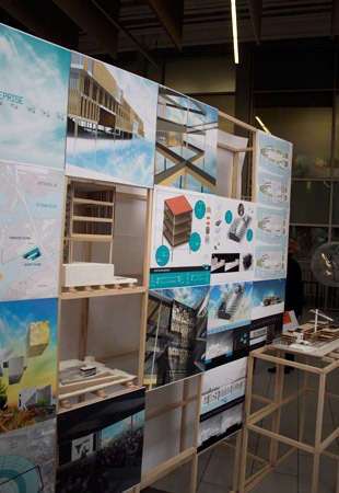 Pictured are renderings of the building projects, displayed on wooden scaffolding. The renderings show the building in various stages of development, as well as bisecting some of the building framework.