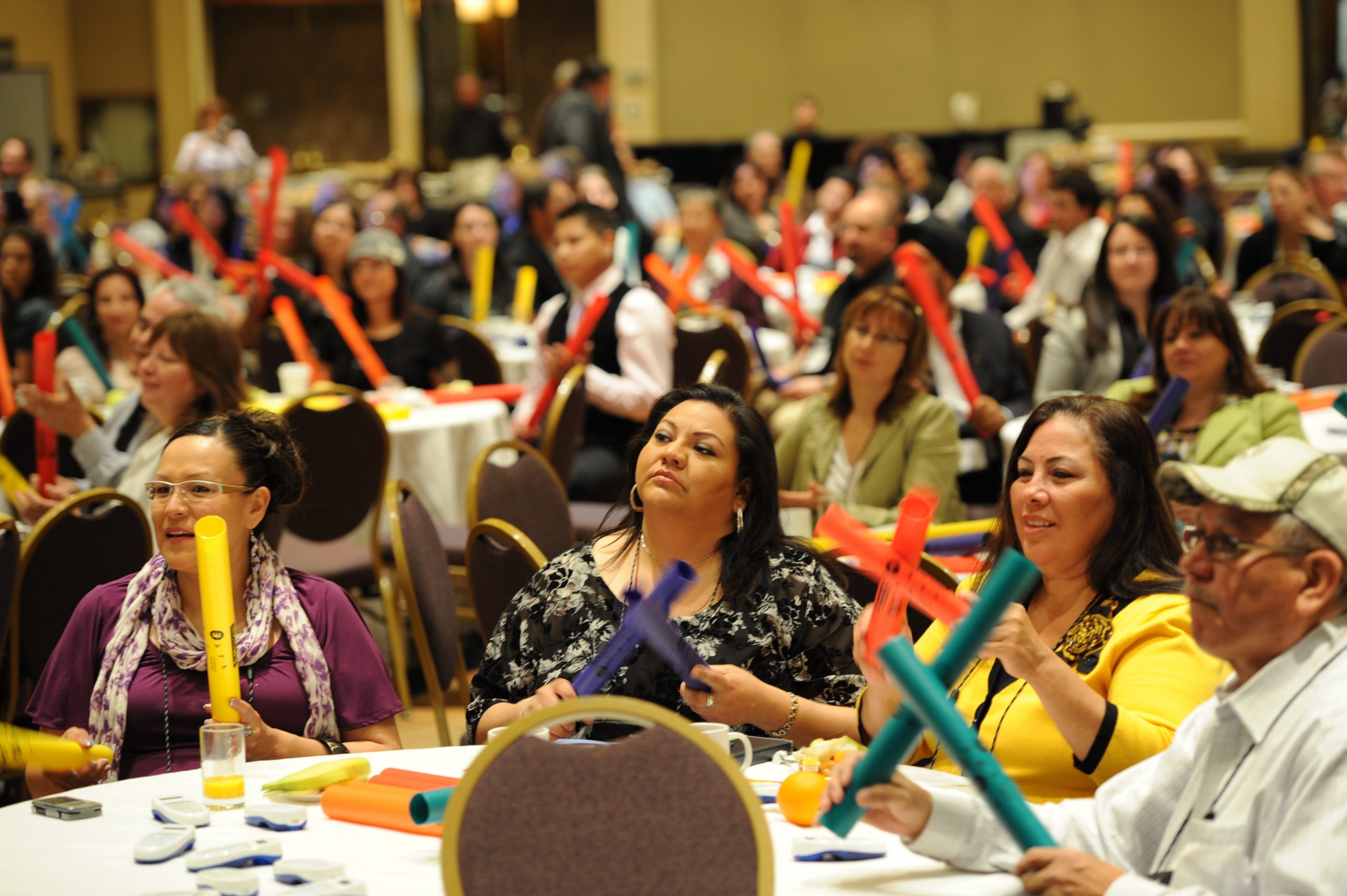 People sitting around round tables, holding colourful cylindrical tubes in their hands.