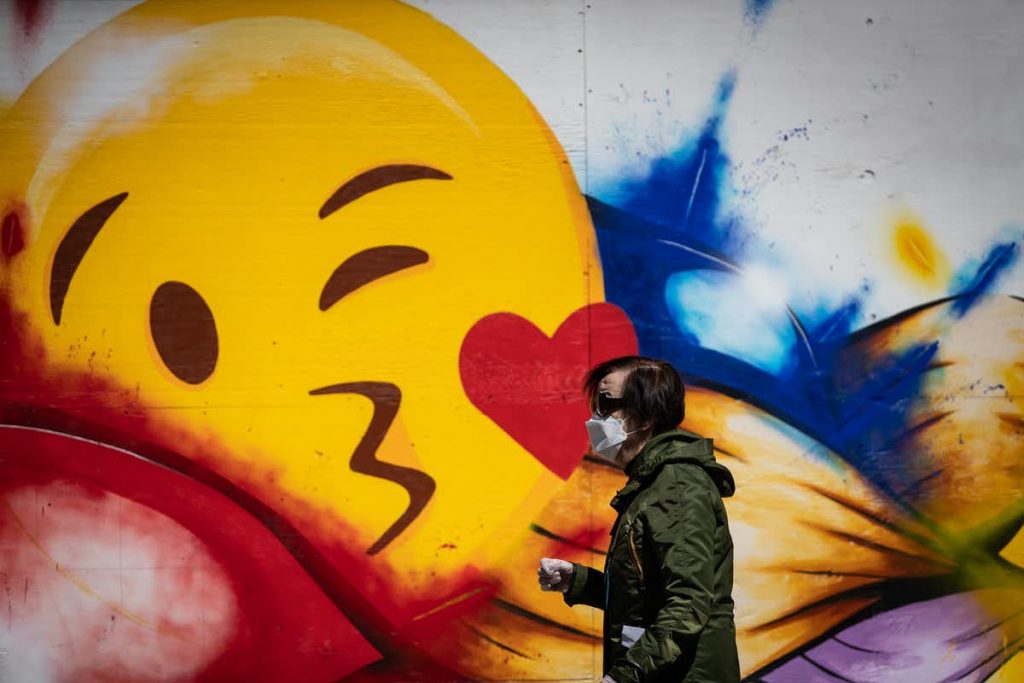 A man wearing a protective face mask and gloves walks past a large emoji face painted on the boarded-up windows of a store on Robson Street, in Vancouver, in May 2020. THE CANADIAN PRESS/Darryl Dyck