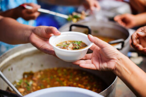 Hands exchanging bowl of lentils and bean stew soup.