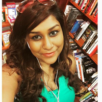 Priya in a green top with sunglasses in her hair and against a bookshelf
