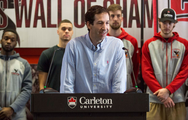 Coach Rob Smart at the Carleton podium with the basketball team behind him