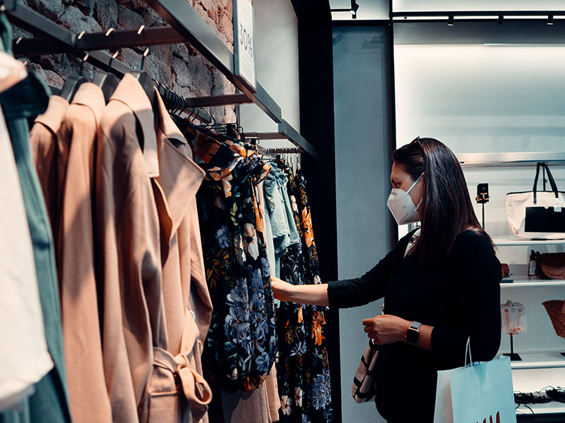 Female shopping wearing a mask in a clothing boutique.
