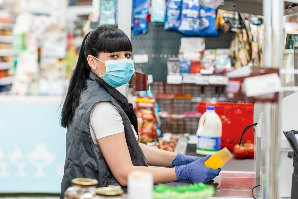 An employee in PPE working at a cash register.