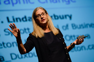 photo of Sprott professor Linda Duxbury standing on the stage. In the background is the powerpoint slide going along with her presentation. 