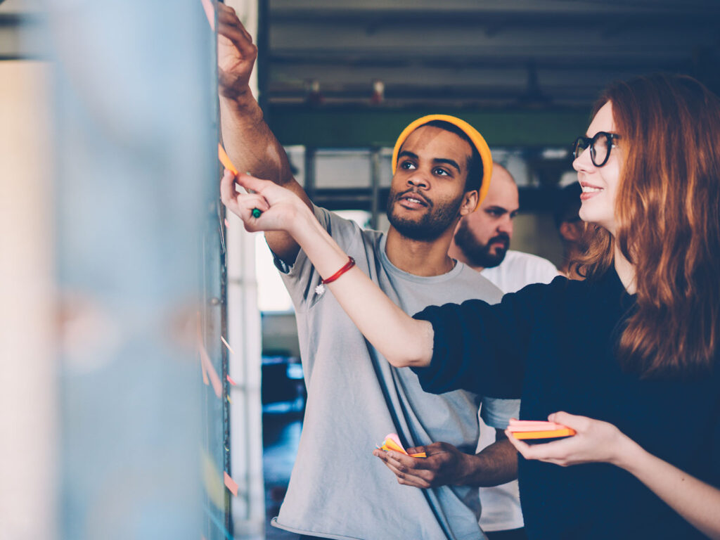 Male and female students adding sticky notes to a whiteboard.